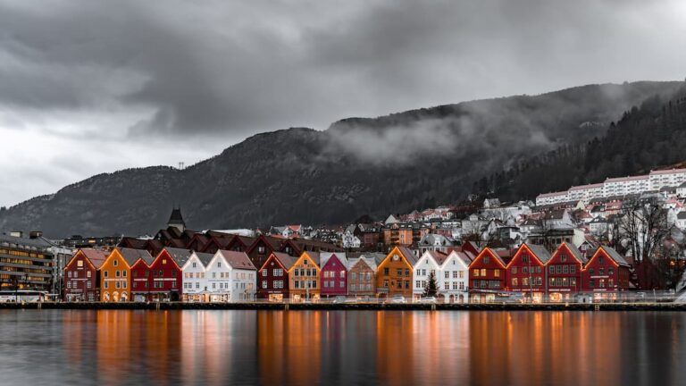 casitas marrones a orillas de un fiordo y montaña detrás en bergen, algo que ver en noruega