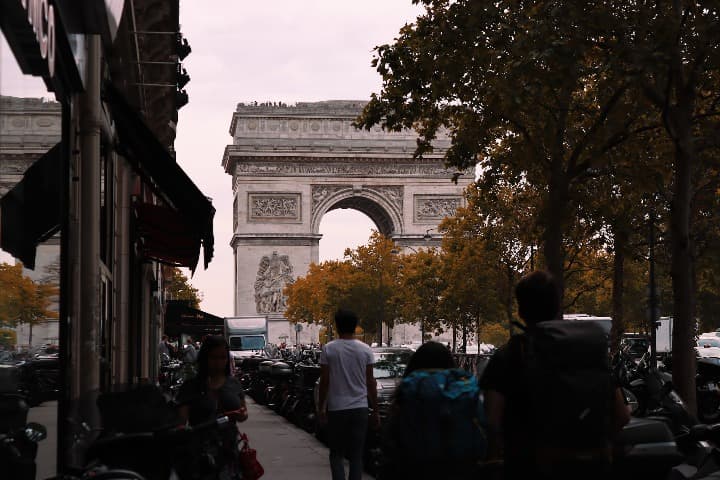 arco de triunfo detrás de árboles en parís, personas de espaldas caminando - weroad