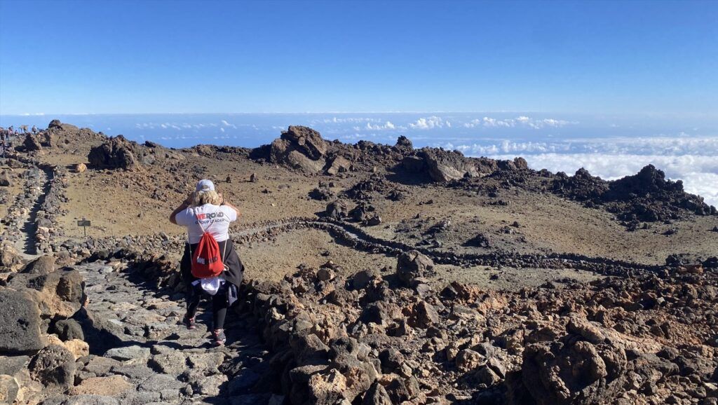 chica de espaldas con camiseta y mochila de weroad caminando por una montaña en tenerife, paisaje seco