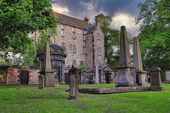 lápidas y edificio detrás en medio de cesped verde en edimburgo - weroad