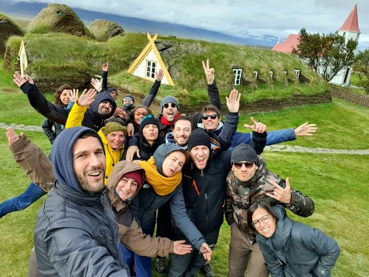 selfie de viajeros weroad en escocia con detrás casas típicas del país con techo cubierto de cesped