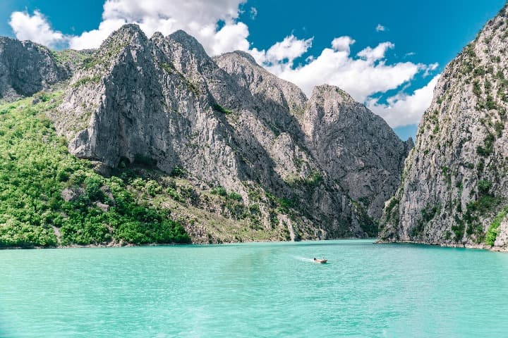 lago de komani en albania, montaña detrás, barquito en el agua - weroad