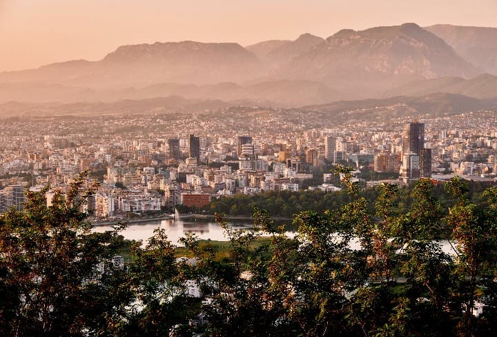 panorama urbano y del lago de tirana con cielo rosa y montañas al fondo - weroad