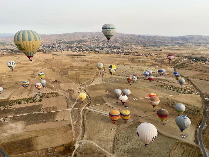 globos aerostaticos volando en el cielo, al fondo la tiera de capadocia, campos y pueblo - weroad