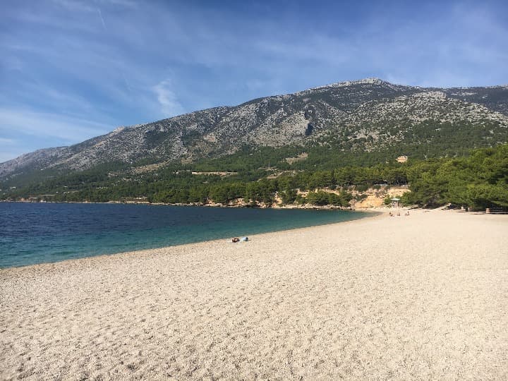 amplia playa en brac, detrás montañas y bosque en craocia - weroad