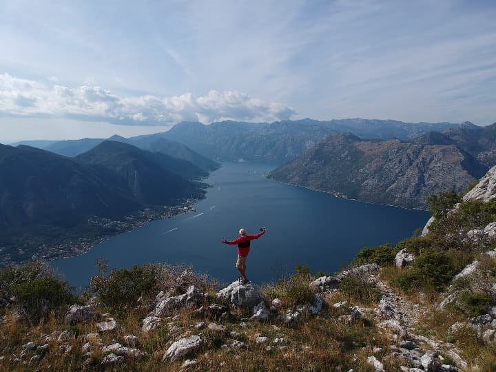 persona con brazos abiertos en medio de montañas que miran hacia una gran cantidad de agua en Boka Kotorska, montenegro - weroad