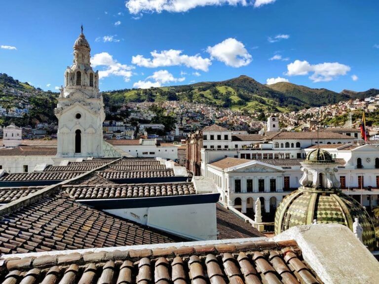 vista de techos de edificios en quito, algo que ver en ecuador, al fondo montaña verde y cielo, se aprecia un campanario de una iglesia - weroad