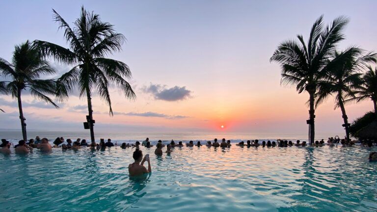 palmeras y agua con gente admirando la puesta del solo en una de las mejores playas de bali - weroad