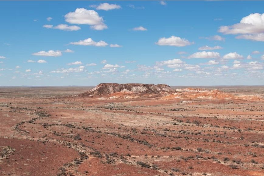 extensión desértica con en medio una montaña, detrás cielo azul con nubes en australia - weroad