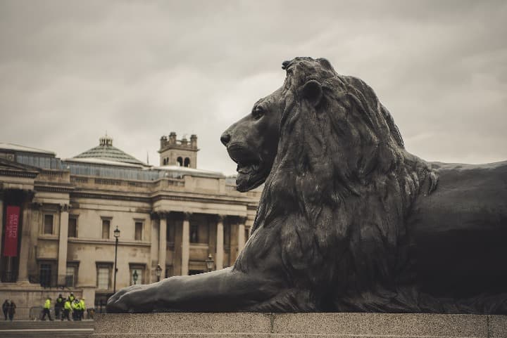 estatua de leon y edificios detrás en trafalgar square, algo que ver en londres - weroad