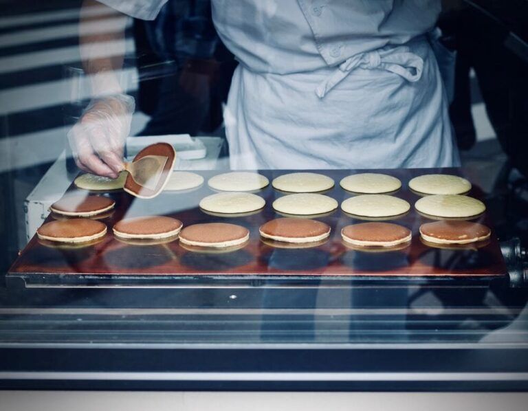 Dorayaki cocinandose encima de una plancha vistos desde un escaparate mientras un cocinero los remueve - weroad