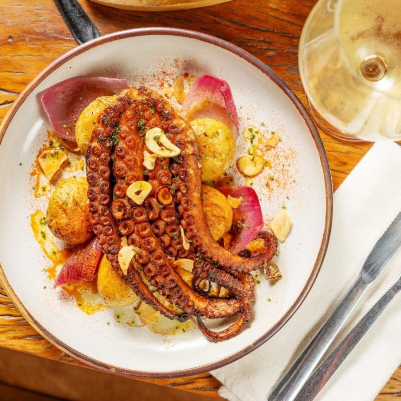 plato de Polvo à lagareiro, pulpo con patatas de fondo, un plato de la comida tipica de portugal 