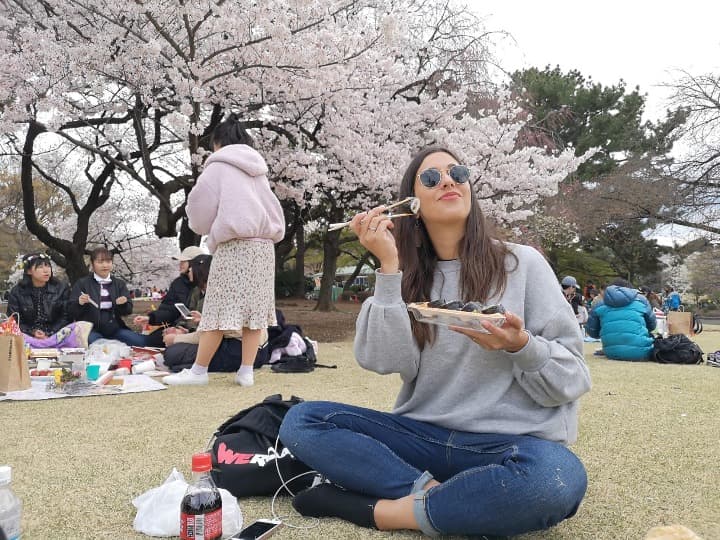 viajera de weroad sentada en un parque con cerezos en flor comiendo sushi, comida tipica de japon