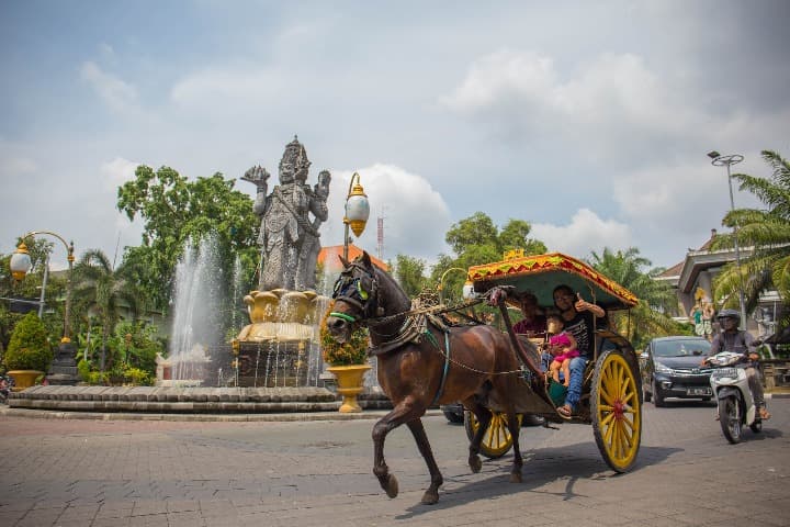 Tuk tuk con caballo y estatua detrás en una plaza de bali
