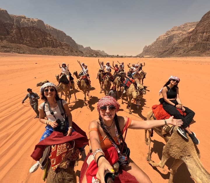 selfie de viajeros de weroad en el desierto, encima de camellos. es seguro viajar a jordania