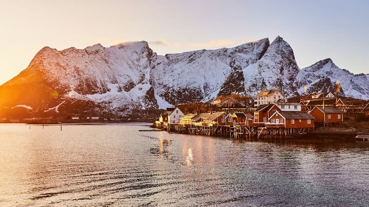 casitas y montaña de fondo con sol a la izquierda en las islas lofoten, donde ver el sol de medianoche