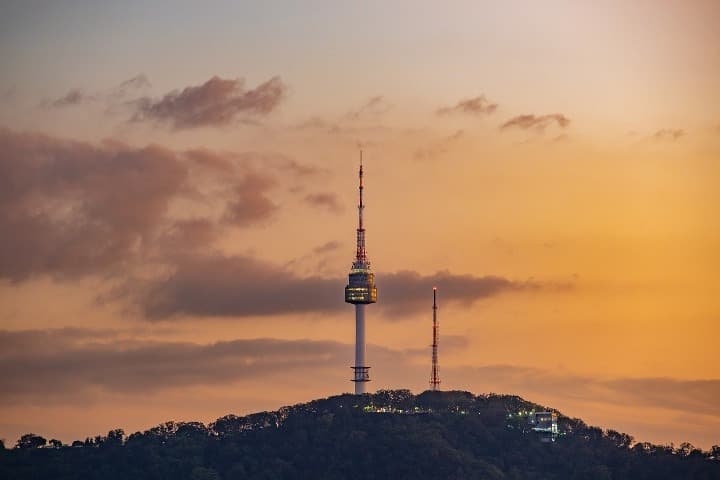 Namsan Tower encima de una montaña, cielo anaranjado detrás, algo que ver en seul