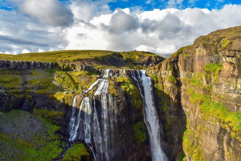 Cascada de Glymur, cielo azul y superfice rocosa verde a los lados