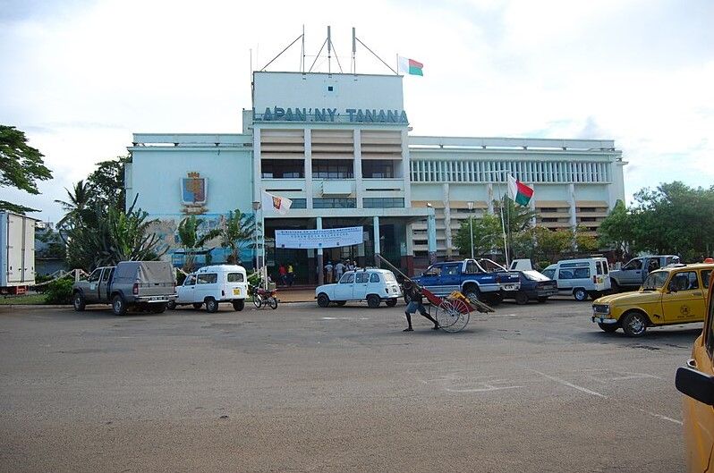 edificio azul claro en Antsiranana, persona tirando de un carro delante, coches