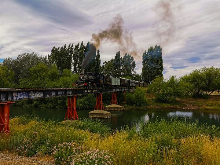la trochita, pasando por un puente en medio de naturaleza verde, uno de los mejores viajes en tren que hacer en argentina