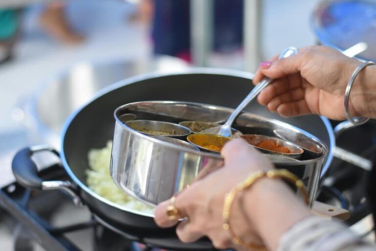 manos de mujer llenando un plato con platos mas pequeños en metal, comida típica india