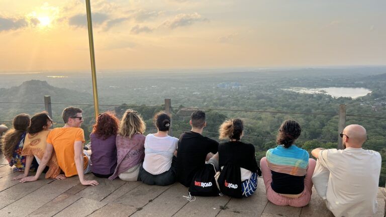 Un grupo de viajeros de WeRoad sentados de espaldas contemplando el atardecer sobre la selva en Sri Lanka.
