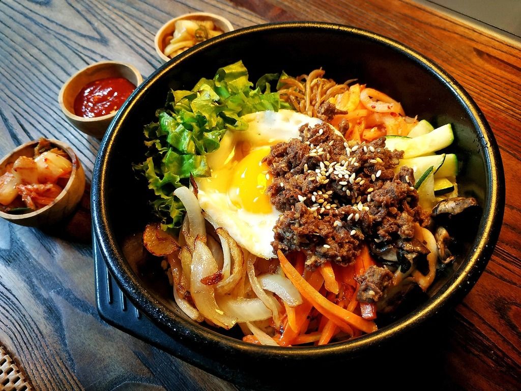 Un delicioso bibimbap con arroz, verduras, huevo y carne, servido con guarniciones coreanas.
