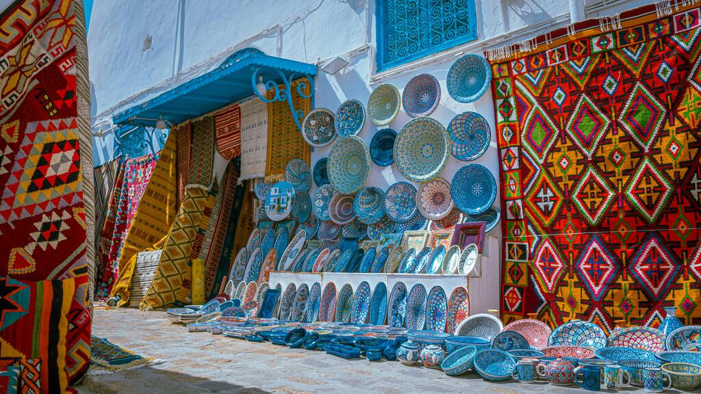 Mercado tunecino con cerámica azul y alfombras de colores vibrantes.