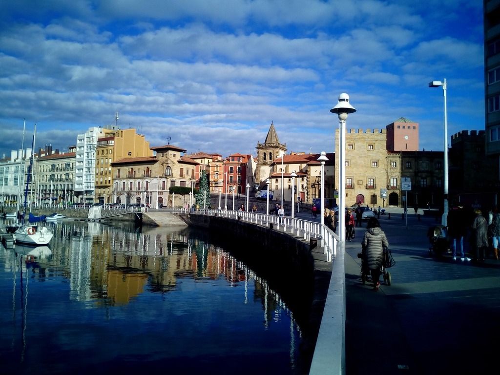 Puerto deportivo y casco histórico de Gijón, Asturias – Vista panorámica del puerto con edificios tradicionales reflejados en el agua.