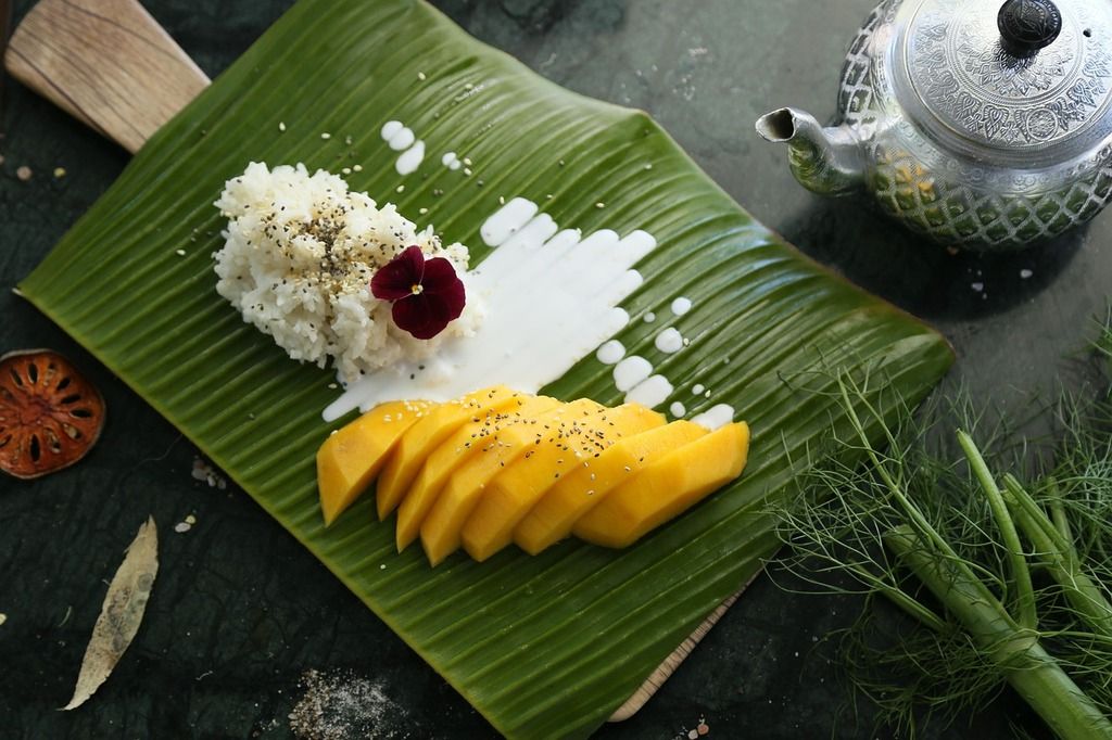 Mango sticky rice, un postre tailandés con arroz glutinoso y leche de coco, presentado sobre una hoja de plátano.