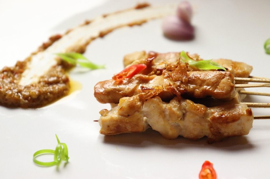 Brochetas de satay de pollo con salsa de cacahuete, presentadas en un plato elegante.