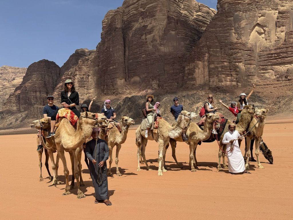Excursión en camello en Wadi Rum, grupo de turistas montando dromedarios con guías beduinos en un desierto de arena roja.