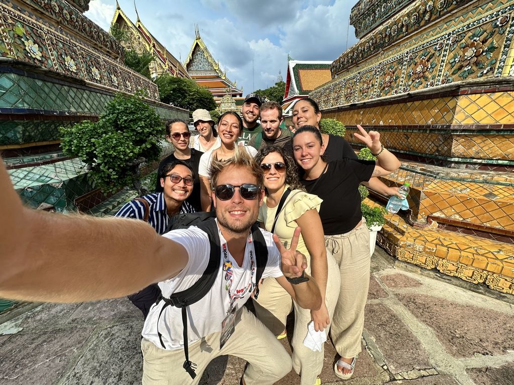 Grupo de viajeros en un tour organizado por WeRoad en Tailandia, posando frente a un templo con detalles dorados y coloridos.