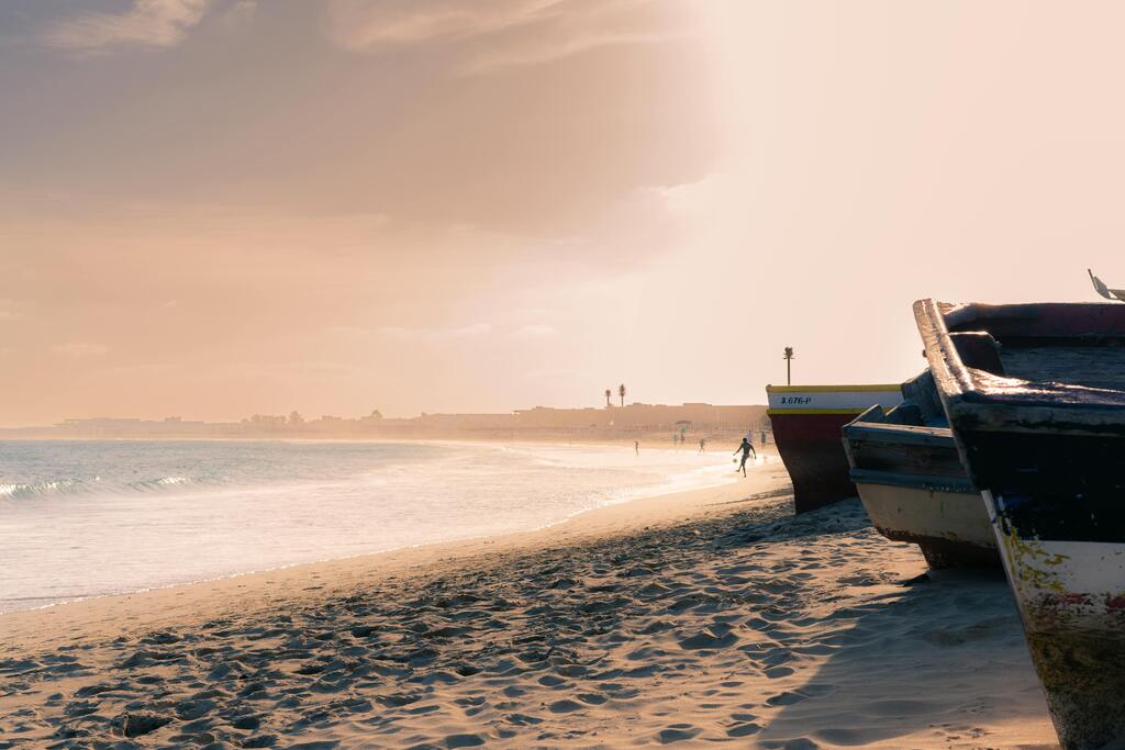 Vista de la playa de Cabo Verde al atardecer con barcas de pesca, mirando hacia la isla de Sal