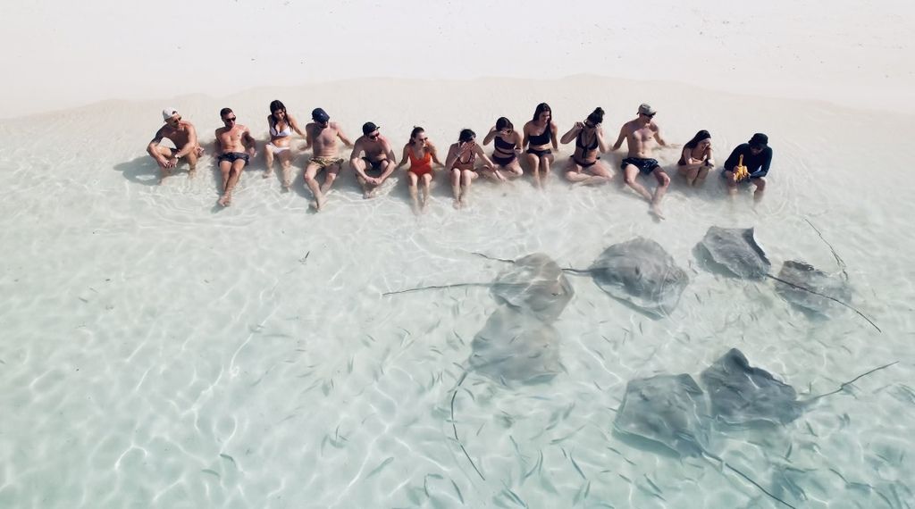 Grupo de viajeros de WeRoad sentado en aguas cristalinas rodeados de mantarrayas en las Maldivas.