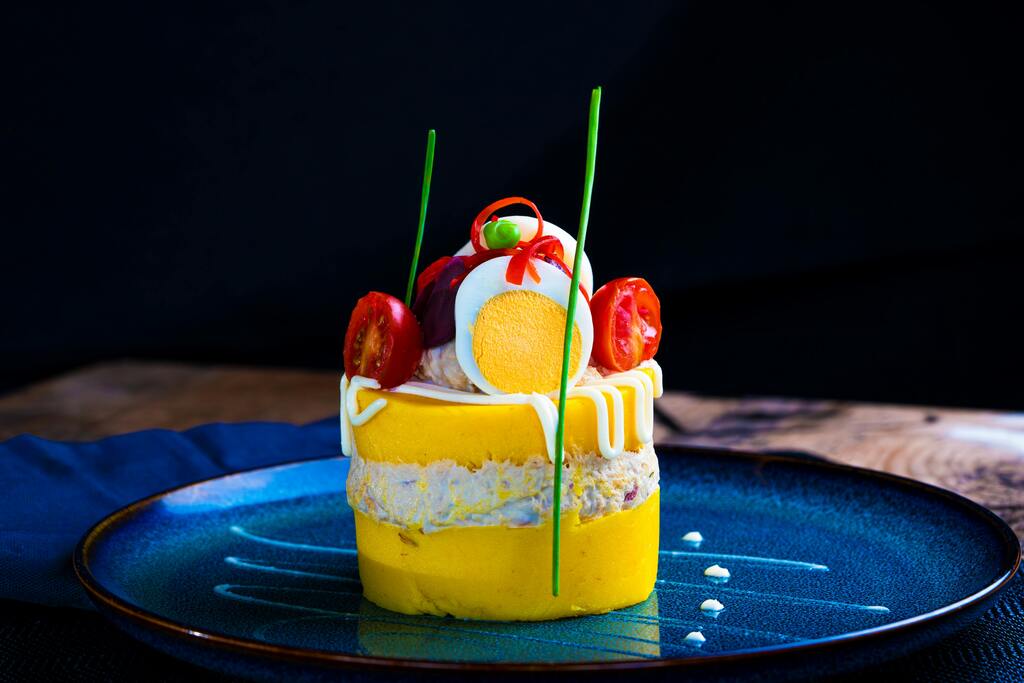 Causa limeña decorada con huevo, tomate y salsa especial.