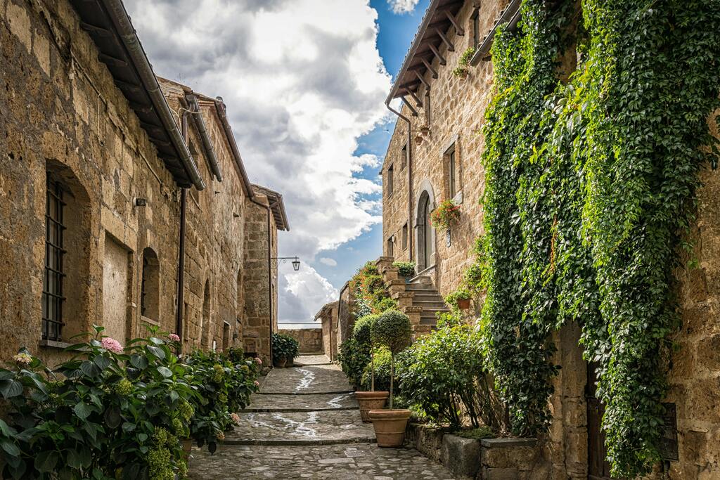 Callejón florido en Pienza, rodeado de casas de piedra y macetas.