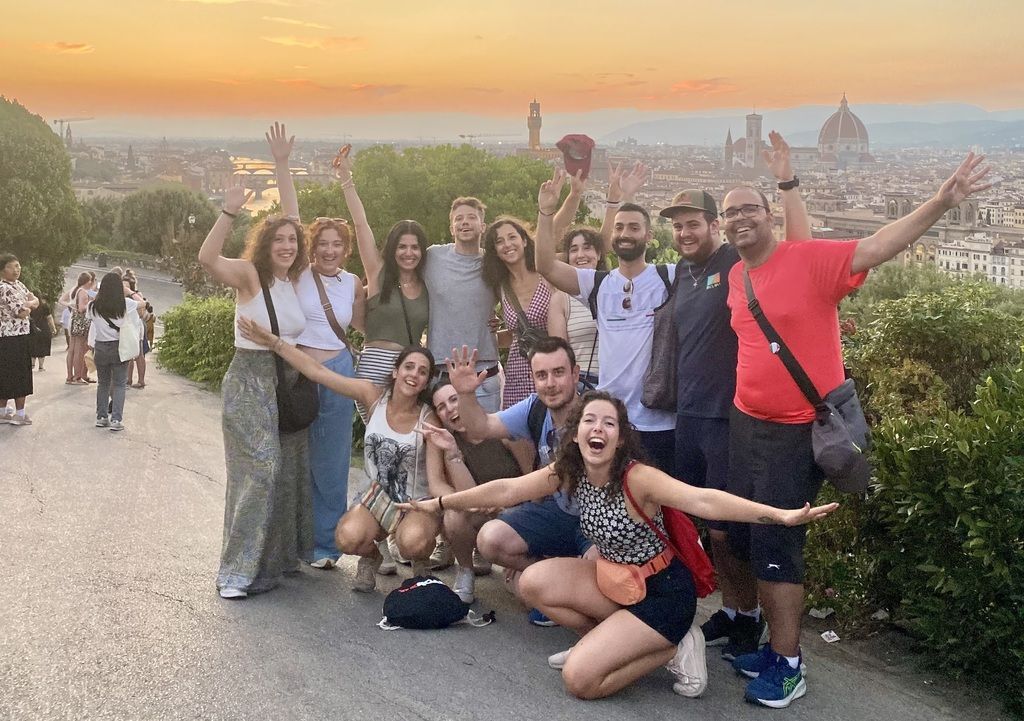 Grupo de viajeros de WeRoad posando con entusiasmo y alegría en un mirador panorámico de Florencia al atardecer, con la cúpula del Duomo y el horizonte de la ciudad al fondo.