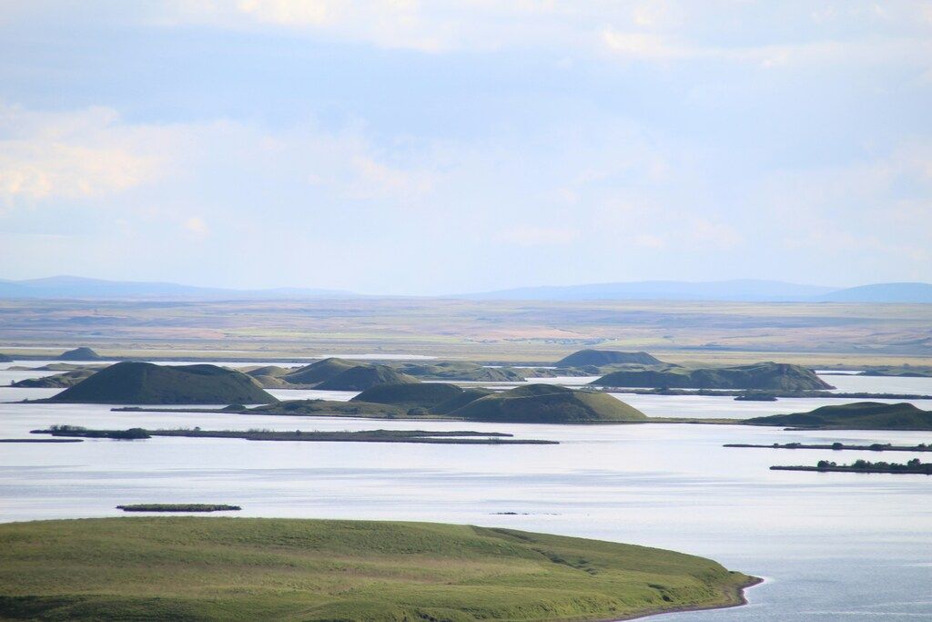 Paisaje sereno del lago Mývatn con formaciones volcánicas verdes en Islandia