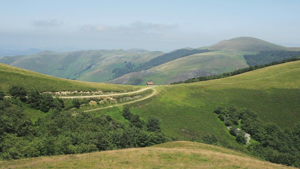 Paisaje de colinas verdes en el norte de España con un camino rural que serpentea entre los valles.