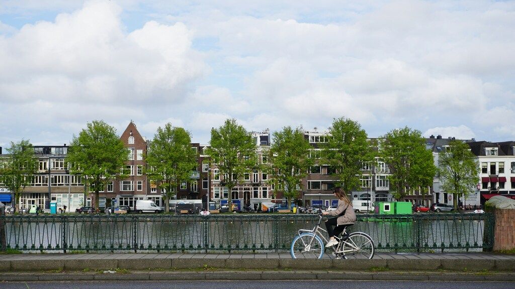 Mujer en bicicleta cruzando un puente en Ámsterdam con casas tradicionales de fondo.