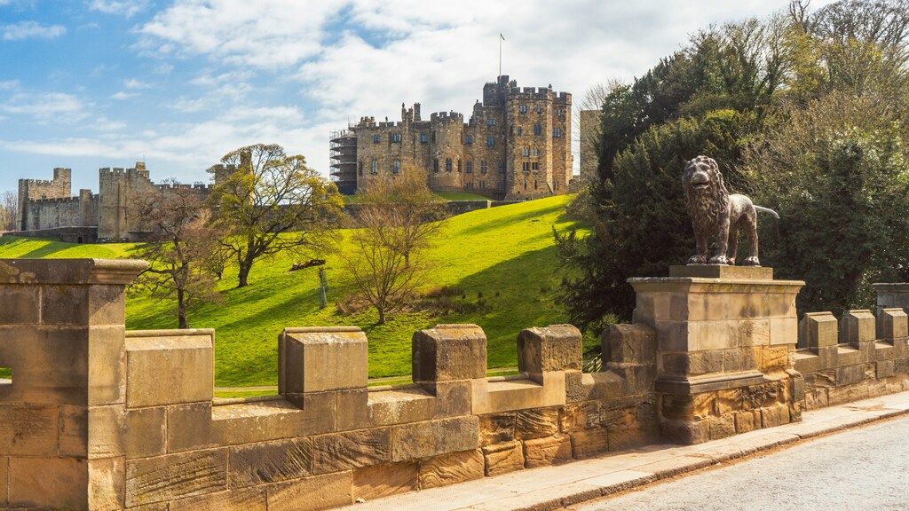 Vista del castillo de Alnwick con una estatua de león en primer plano y colinas verdes.