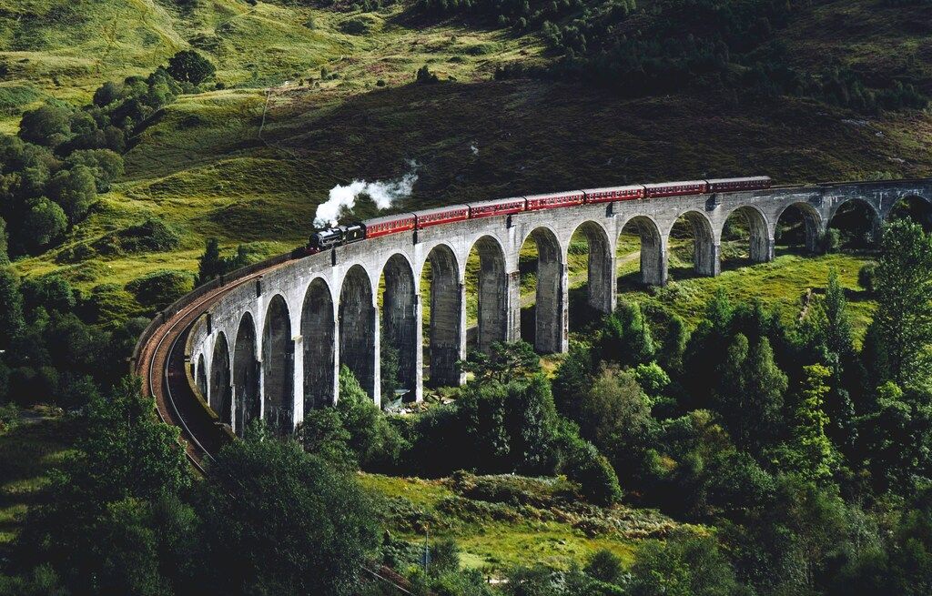 El tren Jacobite cruza el viaducto de Glenfinnan entre verdes colinas escocesas.
