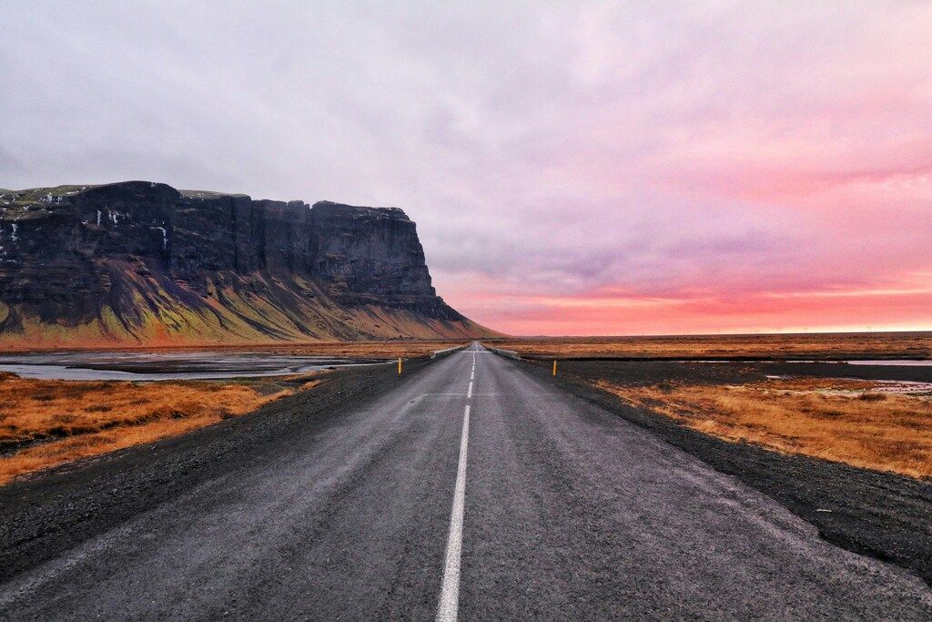 Carretera recta hacia el horizonte con acantilado al amanecer en Islandia