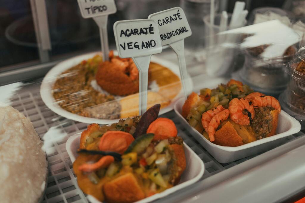 Acarajé tradicional y vegano servido en bandejas dentro de una vitrina de comida típica brasileña