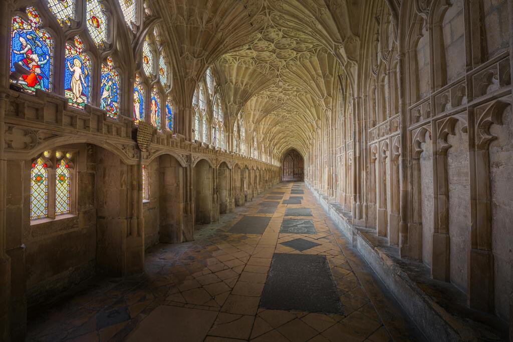 Claustro de la catedral de Gloucester con techos abovedados y vidrieras coloridas.