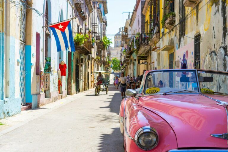 Un convertible rosa clásico aparcado en una calle estrecha y soleada de La Habana con la bandera cubana.