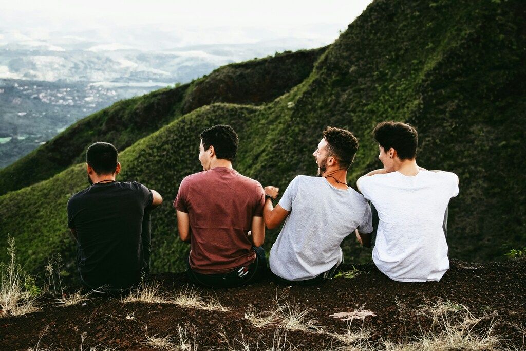 Grupo de amigos sentados en la cima de una montaña, disfrutando de la vista y compartiendo una conversación alegre.