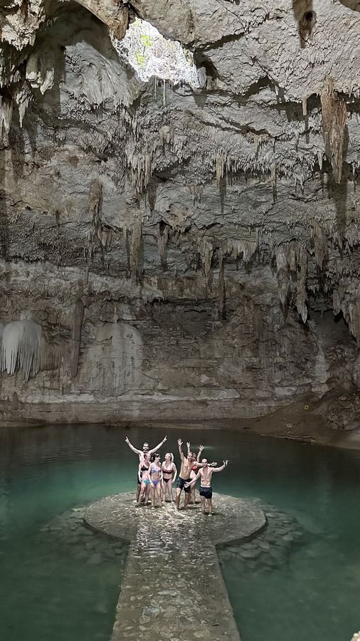 Grupo de personas posando sobre una plataforma circular dentro de un cenote cubierto de estalactitas.