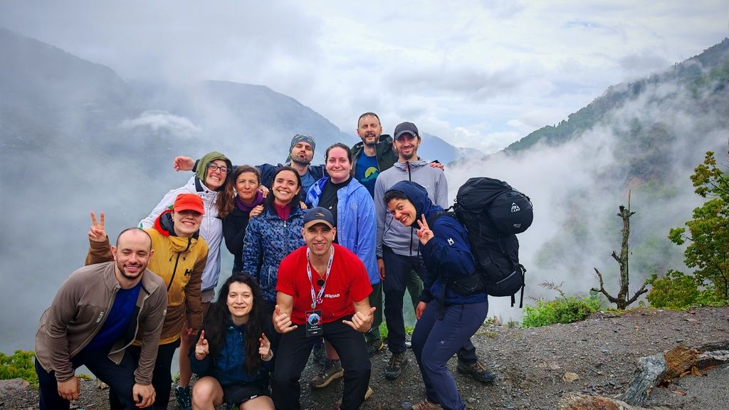 Grupo de viajeros de WeRoad posando felices durante una caminata por la montaña entre nubes y paisajes impresionantes.